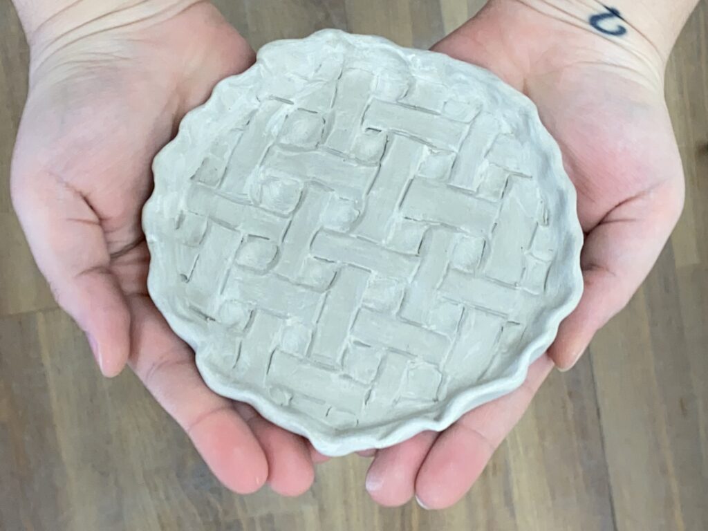 two hands holding a small plate that looks like the top of a pie - in the clay state