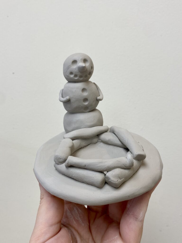 clay snowman sitting in front of a fire pit where the fire pit would fit a tealight candle holder