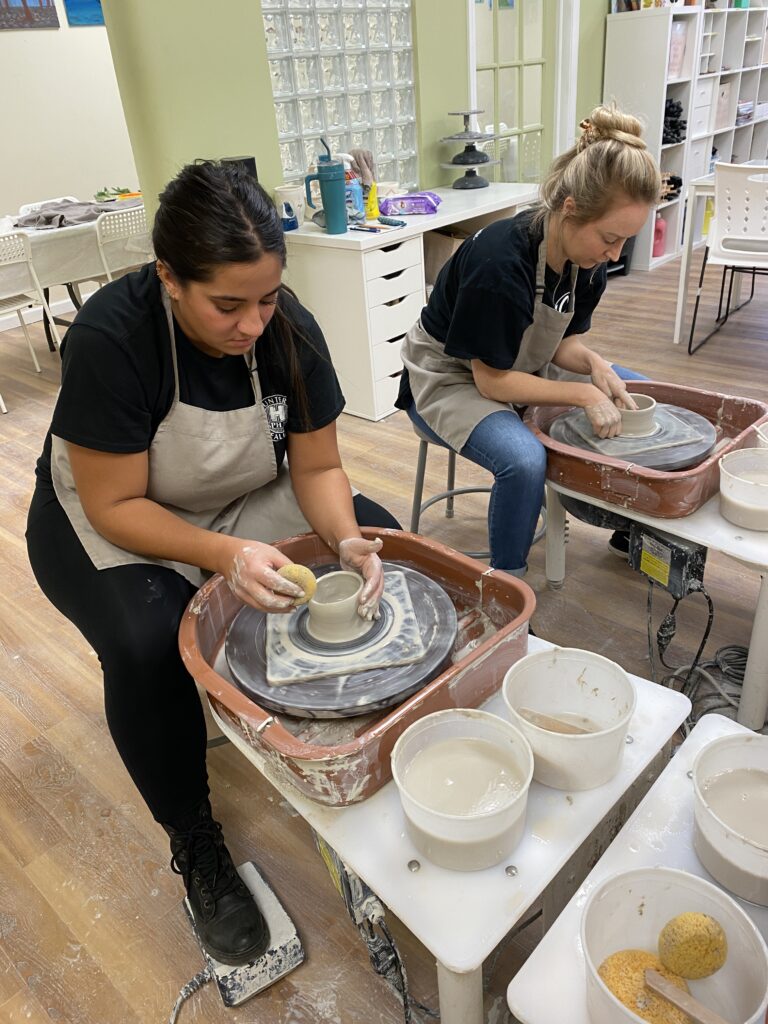 2 young women at the pottery wheel, focused on creating their bowls