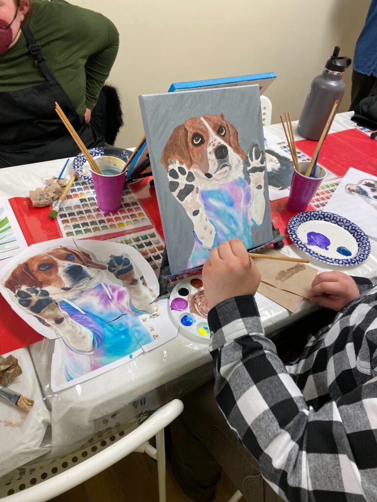 person painting their dog that wears a sweatshirt 