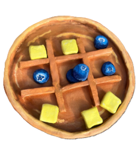 ceramic tic tac toe board that looks like a pancake with butter pats and blueberries as the game pieces
